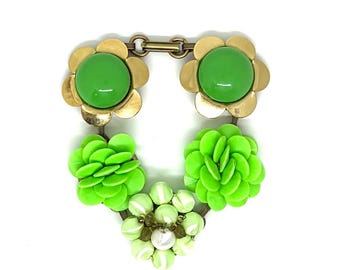 May include: A statement necklace featuring two gold-tone metal flower charms with smooth green cabochon centers, two bright lime green layered petal flower charms, and one central flower charm made of pale green and white striped beads.
