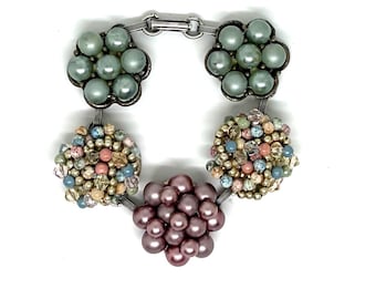 May include: A bracelet featuring five distinct clusters of beads connected by silver-toned metal links. Two clusters consist of light green pearls, two are composed of multicolored small beads and crystals, and one central cluster features mauve pearls.