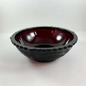 May include: A deep red glass bowl with a scalloped edge and a diamond pattern. The bowl is made of ruby red glass and has a shiny finish.