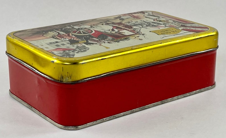 May include: A red and gold tin box with a vintage illustration of a horse-drawn carriage and the text "24 Gold" on the lid.