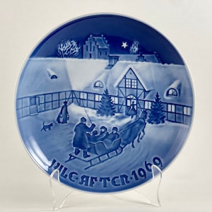 May include: Blue and white Christmas plate with a winter scene of a house, trees, and people riding in a sleigh. The plate has the text "Jul. Aft. Cr. 1969" on the bottom.