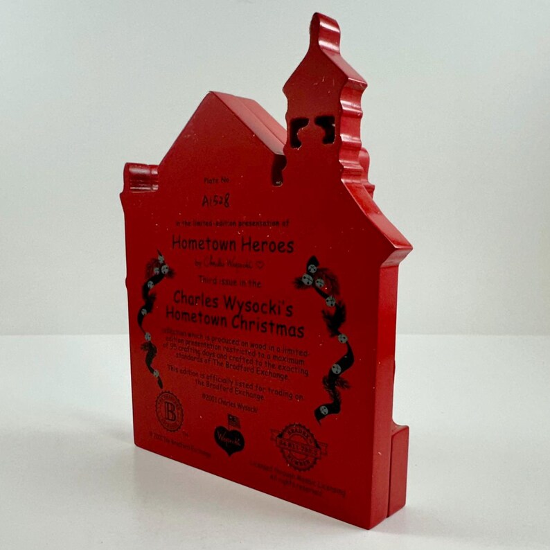 May include: Red wooden Christmas ornament shaped like a house with a white inscription that reads "Part No. A1518 In the spirit of appreciation of Hometown Heroes Third Edition in the Charles Wysocki's Hometown Christmas This ornament is produced in a limited, hand-numbered series. Each ornament is crafted of the finest cast resin, exacting the highest standards of quality. The officially licensed Charles Wysocki's Hometown Christmas 2021 Ornament Series"