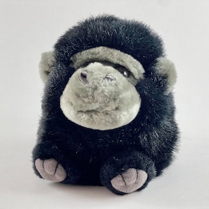 May include: A plush black gorilla toy with a gray face and large, black eyes. The toy is sitting on a white background.