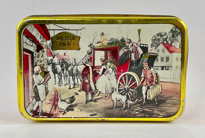 May include: A vintage tin box with a colorful illustration of a horse-drawn carriage arriving at a quaint inn. The sign above the inn reads "Ye Old Inn".