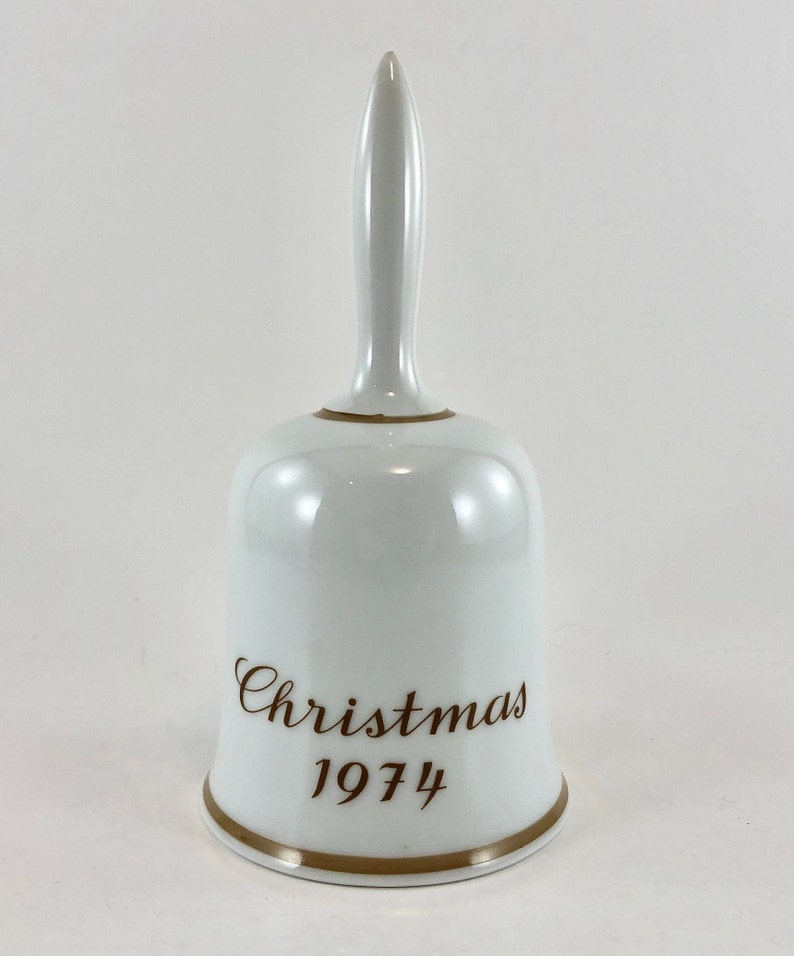 May include: White porcelain Christmas bell with a gold trim and the words "Christmas 1974" in brown lettering.