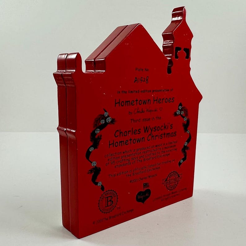 May include: Red wooden house-shaped ornament with a white inscription that reads "Plate No. A1528 In the limited-edition presentation of Hometown Heroes by Charles Wysocki Third issue in the Charles Wysocki's Hometown Christmas collection which is produced in a limited edition presentation featuring the artwork of 95 crafting artists and is considered a treasured piece of the American tradition. This ornament is officially licensed by the Bradford Exchange. 2001 Bradford Exchange"