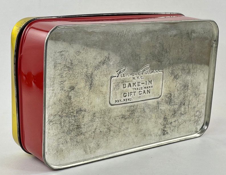May include: Red and yellow metal tin with a silver lid. The lid has the text "Fletcher & Pollack N.Y.C. Bake-In Trade Mark Gift Can Pat. Pend."