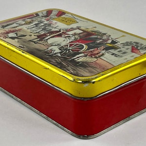 May include: A vintage red and gold tin box with a colorful illustration of a horse-drawn carriage and people in front of a building. The text "Echo Inn" is visible on the box.
