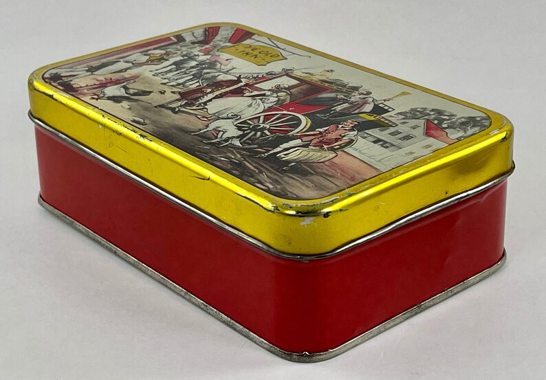 May include: A vintage red and gold tin box with a colorful illustration of a horse-drawn carriage and people in front of a building. The text "Echo Inn" is visible on the box.