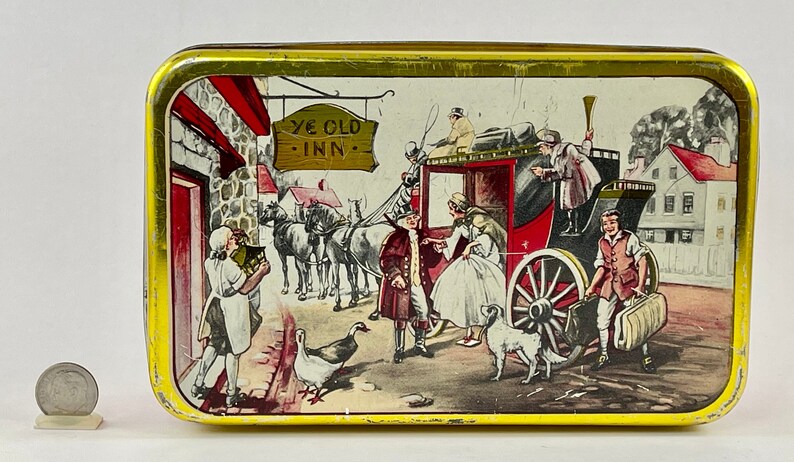 May include: A vintage tin box with a colorful illustration of a horse-drawn carriage arriving at a quaint inn. The sign above the inn reads "Ye Olde Inn".