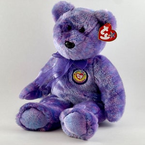 May include: Purple and blue tie-dye plush bear with a purple ribbon around its neck. The bear has a Ty Beanie Baby tag attached to its ear and a Ty Beanie Babies Official Club tag on its chest.
