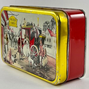 May include: A vintage tin box with a red and gold exterior. The lid features a colorful illustration of a horse-drawn carriage, people, and a sign that reads "Ye Old Inn".