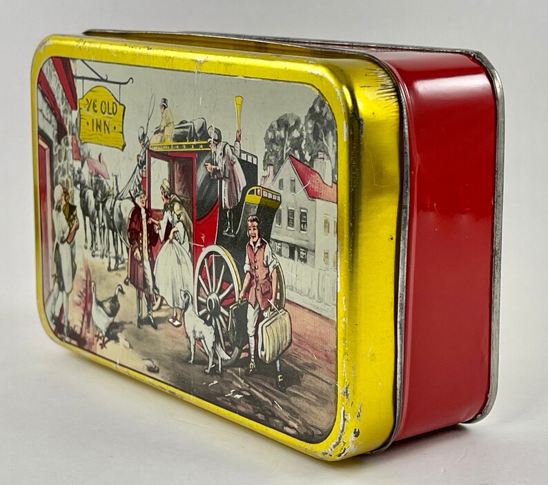 May include: A vintage tin box with a red and gold exterior. The lid features a colorful illustration of a horse-drawn carriage, people, and a sign that reads "Ye Old Inn".
