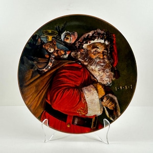 May include: A vintage Christmas plate featuring a jolly Santa Claus carrying a sack of gifts. He is wearing a red suit with white trim and a white beard. The plate has a green background with a gold rim and the date 1-9-8-7.