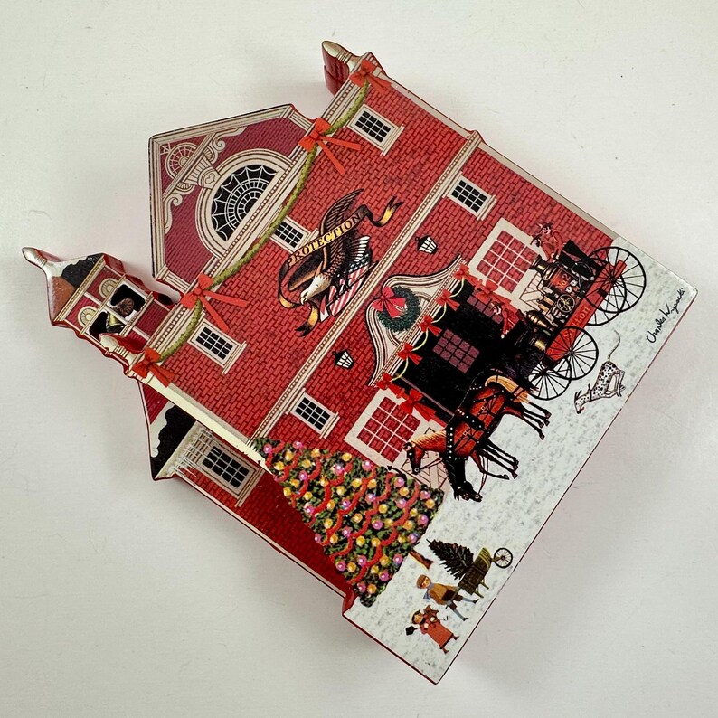 May include: A red and white wooden Christmas ornament shaped like a firehouse with a Christmas tree in front. The firehouse has a bell tower, a sign that says "Protection", and a wreath on the door. There are horses and a carriage in front of the firehouse.