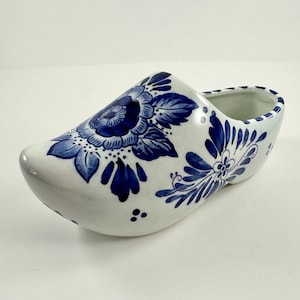 May include: A white ceramic Dutch shoe with blue and white floral designs. The shoe is a traditional Dutch souvenir.