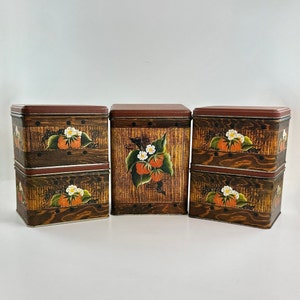 May include: A set of six vintage metal storage tins. The tins have a rectangular shape with a dark brown lid and a wooden-look design. Each tin is decorated with a painted strawberry motif, featuring red berries and white flowers.
