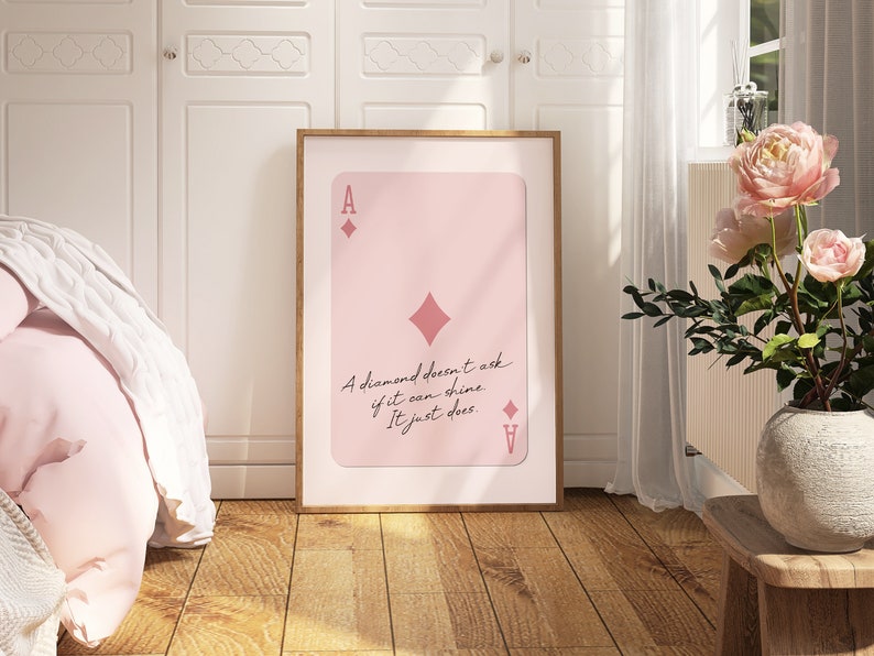 May include: A pink and white printable wall art design featuring an ace of diamonds playing card with the quote "A diamond doesn't ask if it can shine. It just does."