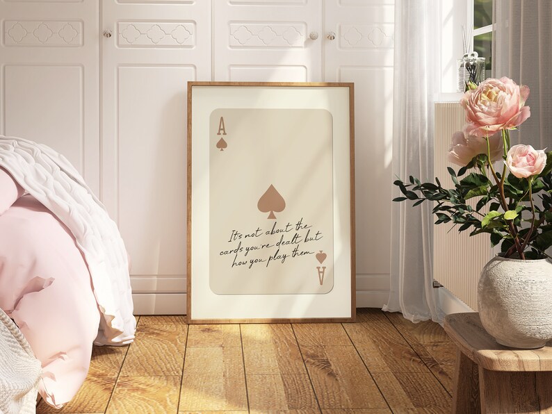 May include: A framed print with a beige background featuring an ace of spades playing card with the quote "It's not about the cards you're dealt but how you play them."