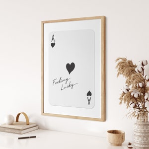 May include: A framed print of an ace of spades playing card with the text "Feeling Lucky" written on it. The card is white with black hearts and the letter A.