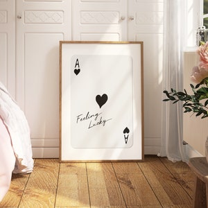 May include: A framed print of an ace of spades playing card with the text "Feeling Lucky" written on it. The card is white with black hearts and the ace symbol.