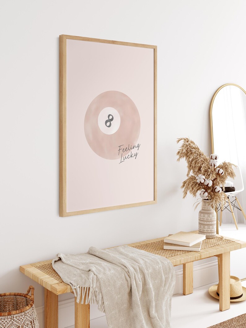 Pode incluir: Uma impress&atilde;o emoldurada com fundo rosa e uma ilustra&ccedil;&atilde;o em aquarela de uma bola de bilhar com o n&uacute;mero 8. O texto "Feeling Lucky" est&aacute; escrito em it&aacute;lico abaixo da bola.