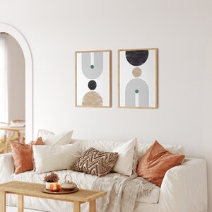 Peut inclure: Deux impressions d'art encadr&eacute;es avec des motifs g&eacute;om&eacute;triques dans un salon. Chaque impression pr&eacute;sente une palette de couleurs beige, noire et verte avec un cadre en bois. Les impressions sont affich&eacute;es au-dessus d'un canap&eacute; blanc avec des coussins d&eacute;coratifs.