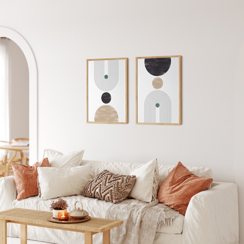 Peut inclure: Deux impressions d'art encadr&eacute;es avec des motifs g&eacute;om&eacute;triques dans un salon. Chaque impression pr&eacute;sente une palette de couleurs beige, noire et verte avec un cadre en bois. Les impressions sont affich&eacute;es au-dessus d'un canap&eacute; blanc avec des coussins d&eacute;coratifs.