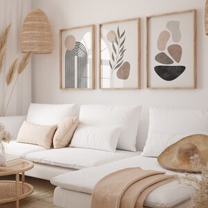 Puede incluir: Un sof&aacute; seccional blanco con una manta de lana beige y un sombrero de paja en la chaise longue. Tres impresiones de arte abstracto cuelgan en la pared detr&aacute;s del sof&aacute;. Las impresiones presentan formas geom&eacute;tricas, una hoja y un arco&iacute;ris.