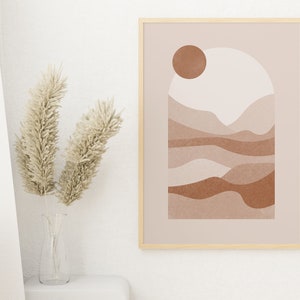 May include: A framed abstract print with a beige background and a brown sun. The print features a stylized landscape with brown and beige hills and valleys.