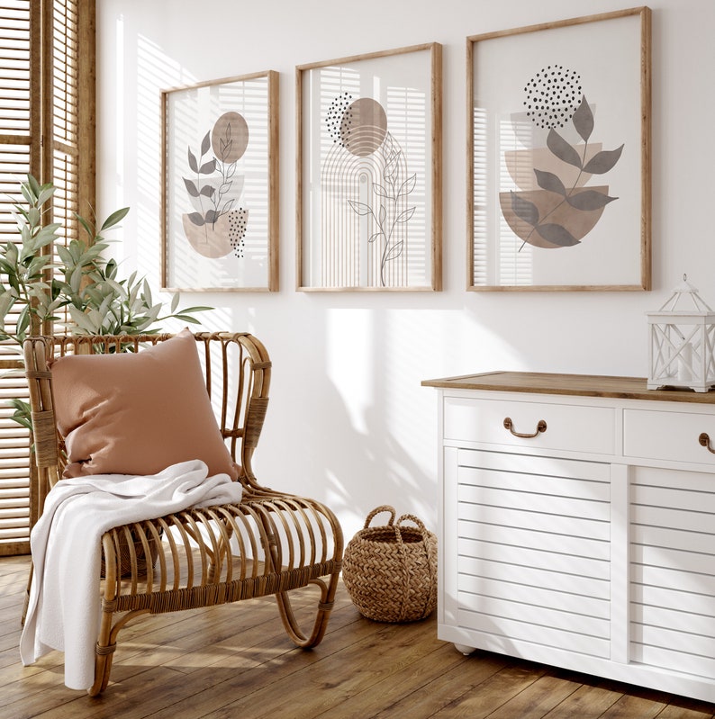 Puede incluir: Un armario blanco con dos cajones y dos puertas, una silla de mimbre con un coj&iacute;n marr&oacute;n y una manta, y tres impresiones enmarcadas con dise&ntilde;os geom&eacute;tricos abstractos en marr&oacute;n y negro.