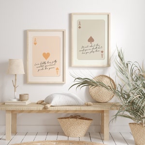 May include: Two framed prints with a light pink and beige background featuring a playing card design with the ace of spades and the ace of hearts. The text on the prints reads "Love boldly, live fully and let your heart guide the game" and "It's not about the cards you're dealt but how you play them".