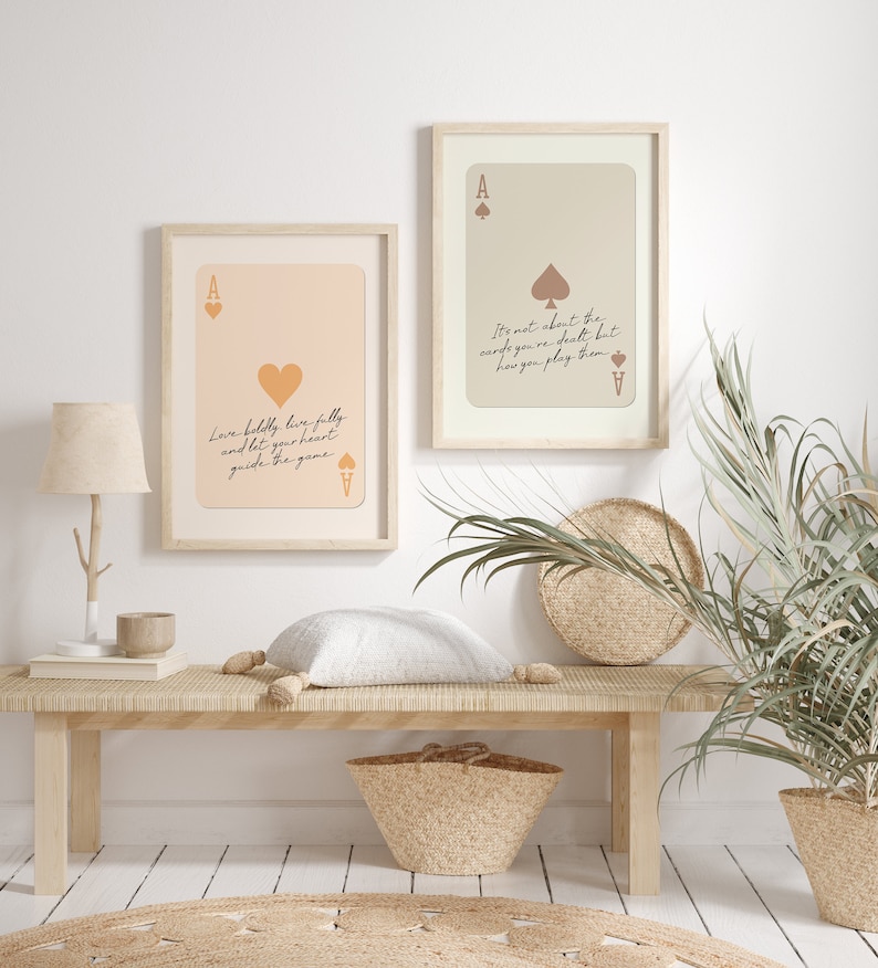 May include: Two framed prints with a light pink and beige background featuring a playing card design with the ace of spades and the ace of hearts. The text on the prints reads "Love boldly, live fully and let your heart guide the game" and "It's not about the cards you're dealt but how you play them".