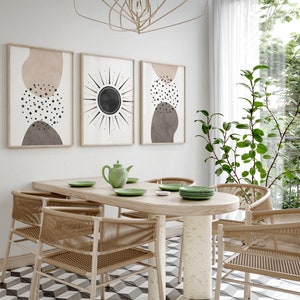 Puede incluir: Un comedor con una mesa de madera ovalada y seis sillas. La mesa es de madera clara y las sillas son de mimbre tejido de color marr&oacute;n natural. Hay tres impresiones de arte abstracto en la pared detr&aacute;s de la mesa. Las impresiones son en tonos de marr&oacute;n, beige y negro. Una tetera verde y cuatro platos verdes est&aacute;n sobre la mesa. La habitaci&oacute;n tiene una pared blanca y una ventana grande con cortinas blancas.