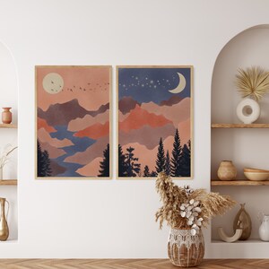 Peut inclure: Deux impressions d'art encadr&eacute;es repr&eacute;sentant des paysages. L'une repr&eacute;sente un coucher de soleil avec un soleil, des oiseaux et des montagnes. L'autre montre une sc&egrave;ne de nuit avec une lune, des &eacute;toiles et des pins. La palette de couleurs comprend des nuances d'orange, de bleu et de marron.
