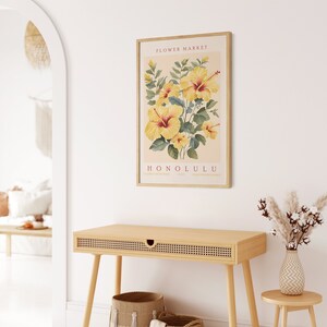 May include: A framed print with a vintage aesthetic featuring a botanical illustration of yellow hibiscus flowers with green leaves. The print has the text "FLOWER MARKET HONOLULU" in red and black lettering.
