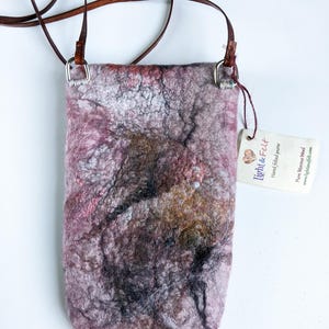 May include: A small, pink, gray, and brown felted crossbody bag with a brown leather strap and silver hardware. The bag has a tag that says "Light & Felt" and "Hand felted purse".