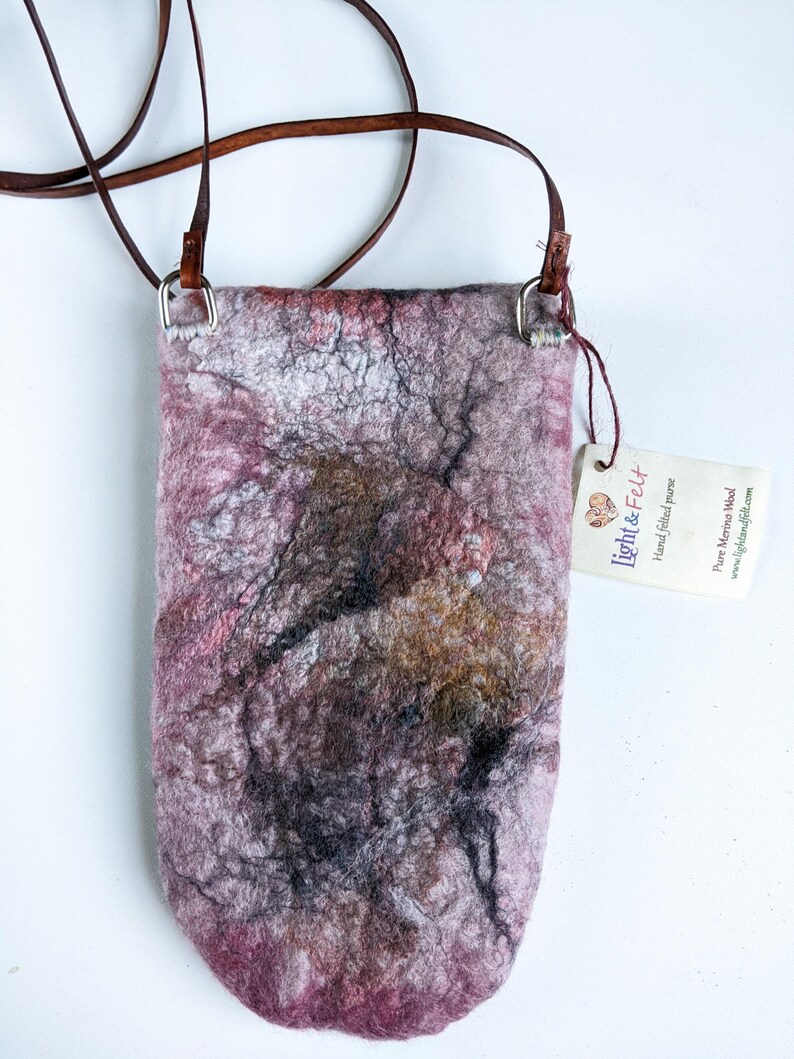 May include: A small, pink, gray, and brown felted crossbody bag with a brown leather strap and silver hardware. The bag has a tag that says "Light & Felt" and "Hand felted purse".