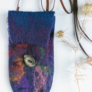 May include: A small, purple and blue felted crossbody bag with a brown leather strap and a wooden button closure.