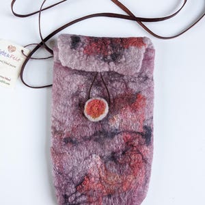 May include: A small, purple, felted bag with a brown leather strap and a red felt button closure. The bag has a mottled, abstract pattern of red, orange, and black.