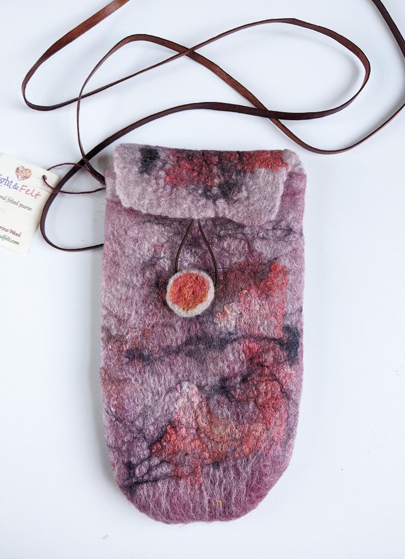 May include: A small, purple, felted bag with a brown leather strap and a red felt button closure. The bag has a mottled, abstract pattern of red, orange, and black.