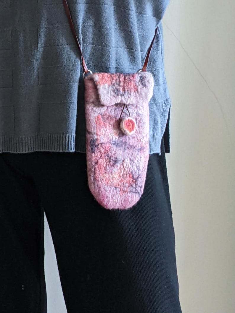 May include: A pink and purple felted wool crossbody bag with a brown leather strap and a small pink pom-pom accent.