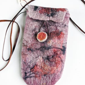 May include: A small, felted bag with a pink, red, and black marbled design. The bag has a brown leather strap and a round, orange button closure. The bag is handmade and has a unique, artistic look.
