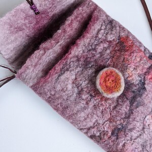 May include: A small, pink and purple felted bag with a brown leather strap and a red felt button.