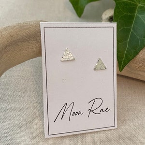 May include: A pair of silver triangle stud earrings on a white card with the text "Moon Rae" written in black.
