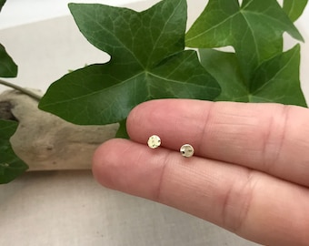 Puede incluir: Un par de pequeños pendientes redondos de color dorado. Los pendientes están martillados y tienen una superficie texturizada.