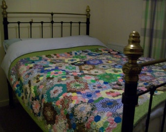 May include: A black metal bed frame with a brass headboard and footboard. The bed is made with a white sheet and a colorful patchwork quilt.