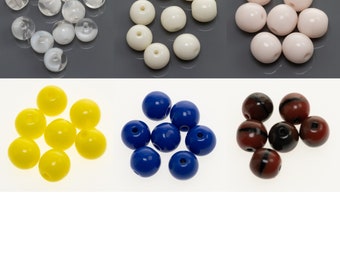 Könnte beinhalten: Sortiment an bunten Glasperlen in verschiedenen Farben, darunter klar, weiß, rosa, gelb, blau und braun mit schwarzen Streifen.