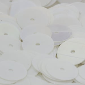 May include: A pile of white round sequins with a hole in the center. The sequins are arranged in a random pattern.