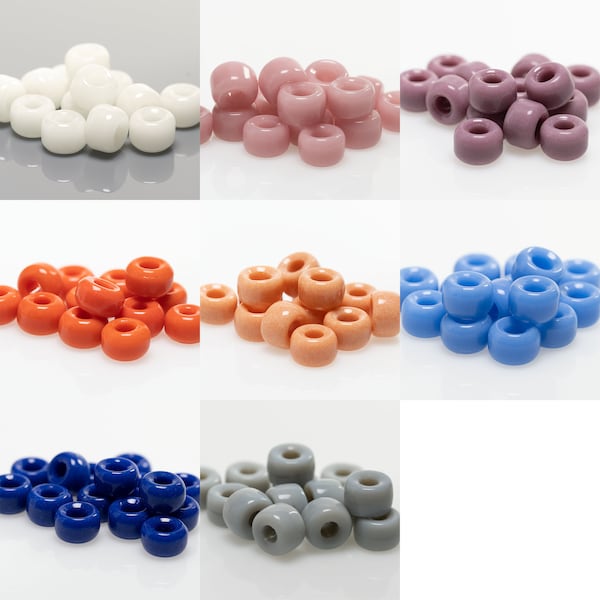 May include: Assortment of round ceramic beads in various colors, including white, pink, orange, peach, blue, gray, and dark blue. The beads are arranged in piles on a white surface.